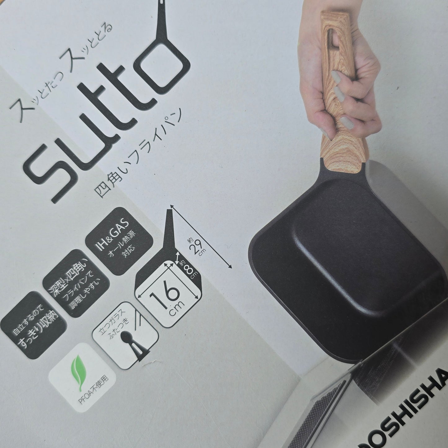 Black frying pan with wooden handle held by a hand, against a white background with 'Sutto' branding.